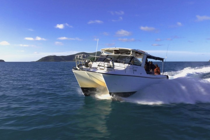 White motorboat speeding on open blue water with distant islands in the background.