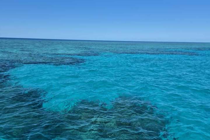 Clear turquoise ocean water with visible coral reef under a blue sky.