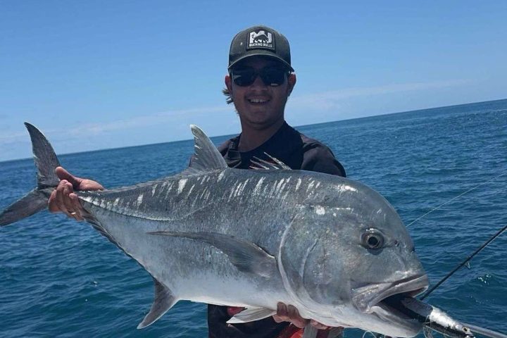 Person on boat holding a large fish against a clear blue sky.