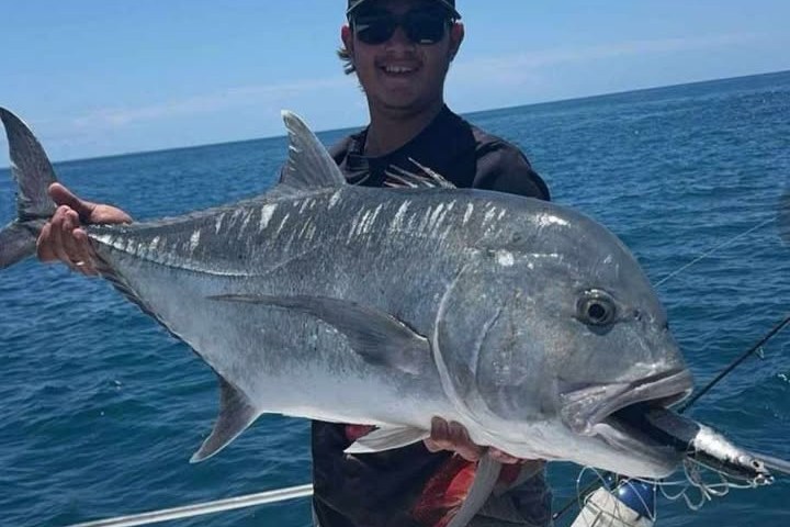 Person on boat holding large fish under clear blue sky.