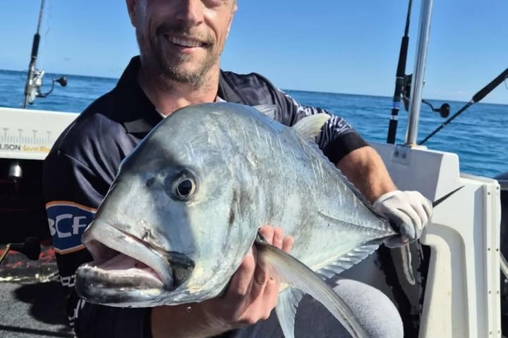 Person on a boat holding a large fish, smiling at the camera.
